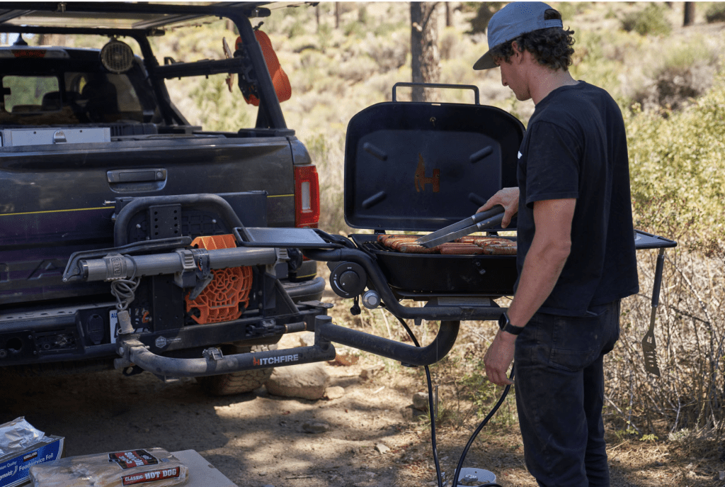 Guy using HitchFire to grill some hotdogs during his outdoor adventure.