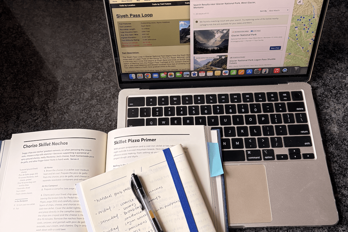 Laptop, notebook, cookbook all being used for planning a camping trip to Glacier National Park